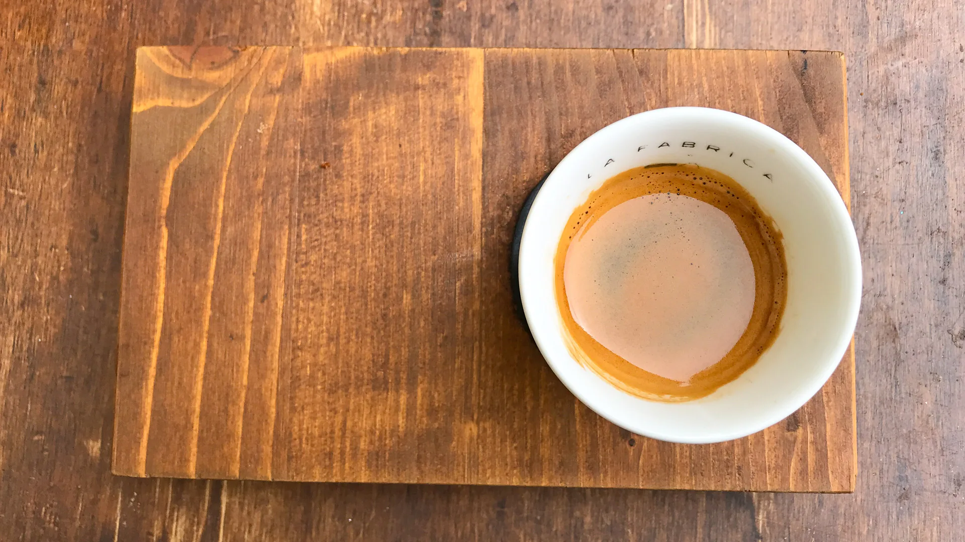 Half-finished espresso in white cup on wooden tray at La Fábrica café in Girona, Spain