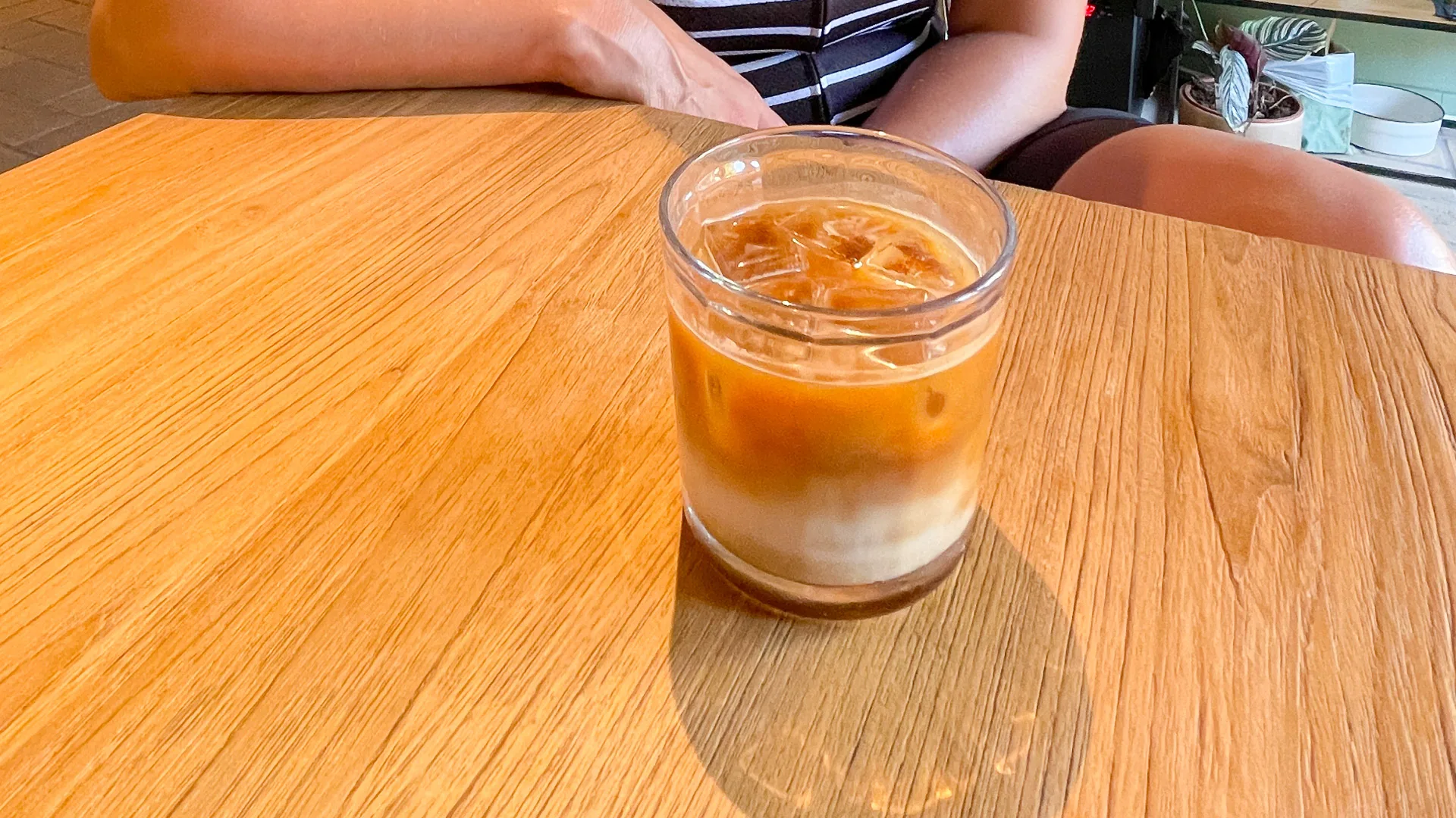 Glass of iced coffee on wooden table at a café in Girona, with person seated in the background