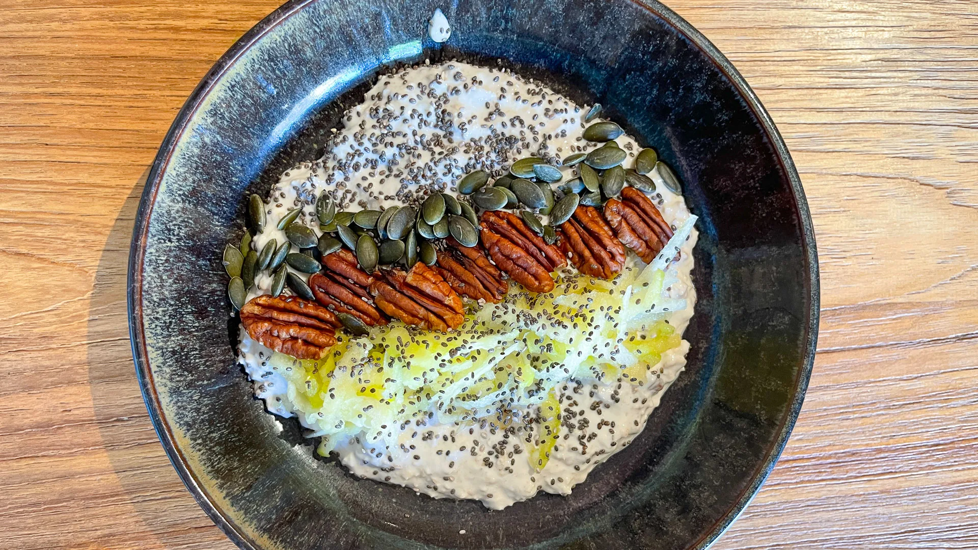 Bowl of oats topped with pecans, pumpkin seeds, chia seeds and olive oil at Girona café