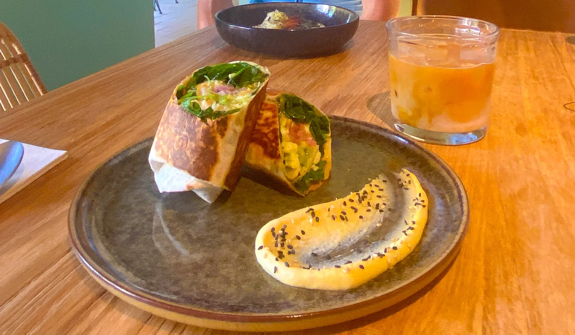 Breakfast wrap with hummus and iced coffee on a ceramic plate at Girona café