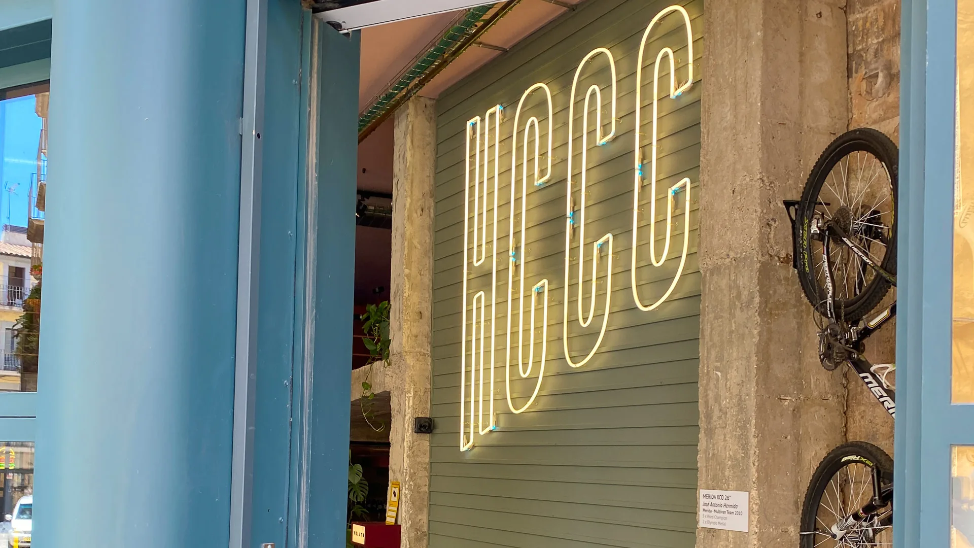 Entrance to Hors Catégorie café in Girona with neon HCCC sign and bikes mounted on the wall