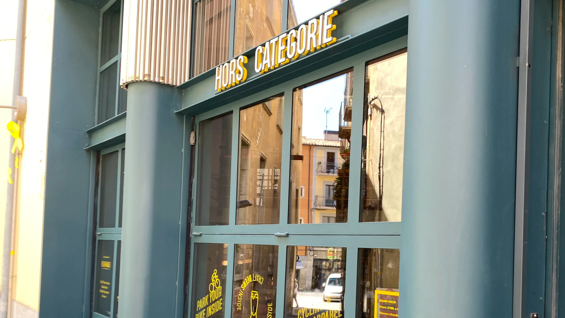 Exterior of Hors Catégorie café in Girona with large glass windows and yellow signage