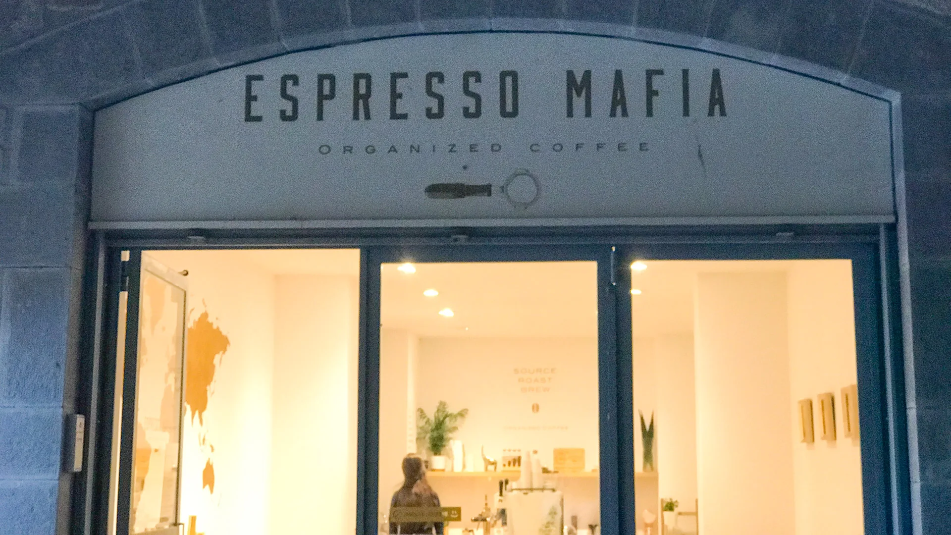 Exterior of Espresso Mafia café in Girona with illuminated minimalist interior and stone archway