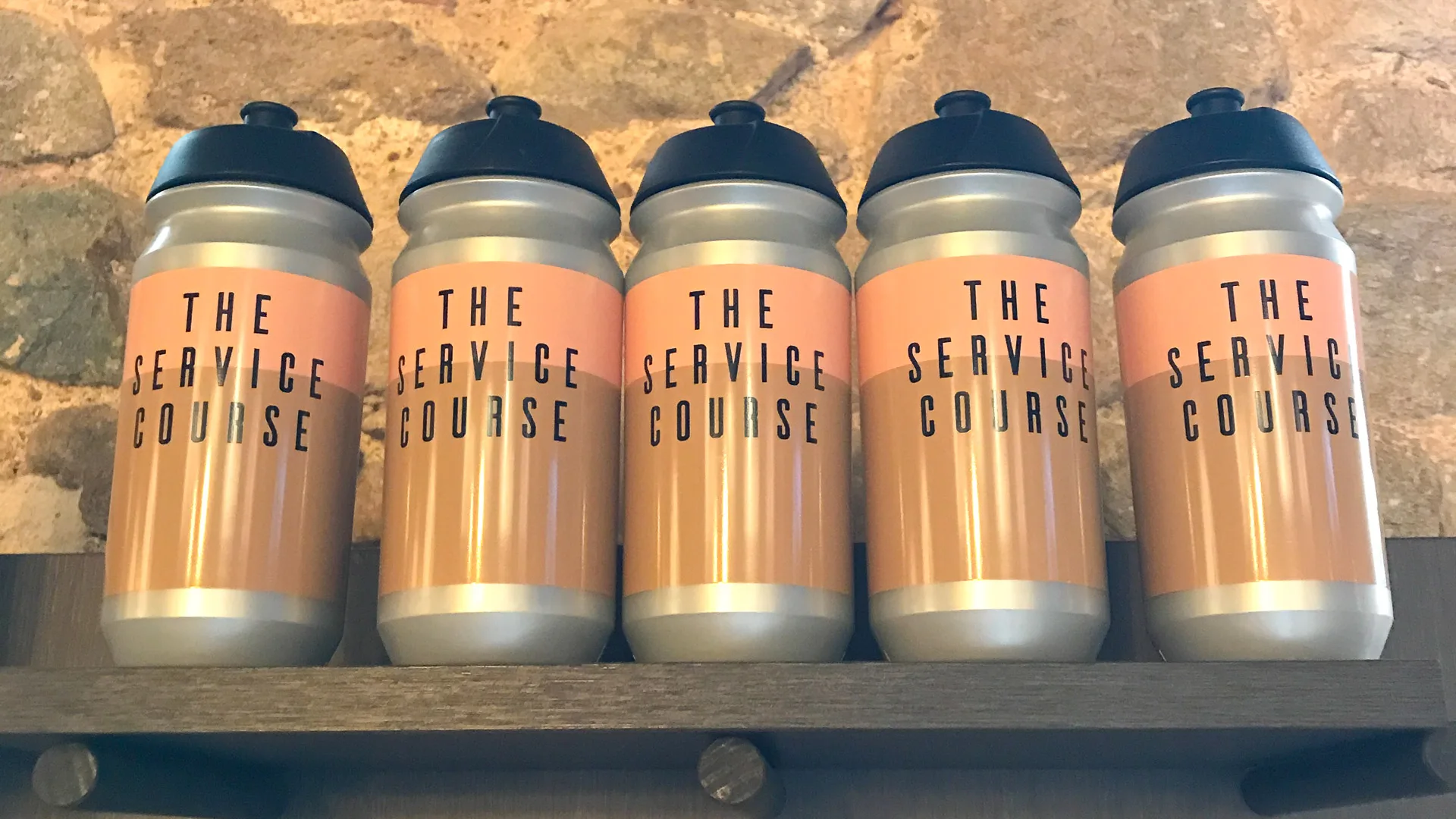 Five pink-labeled water bottles from The Service Course displayed on a shelf in Girona