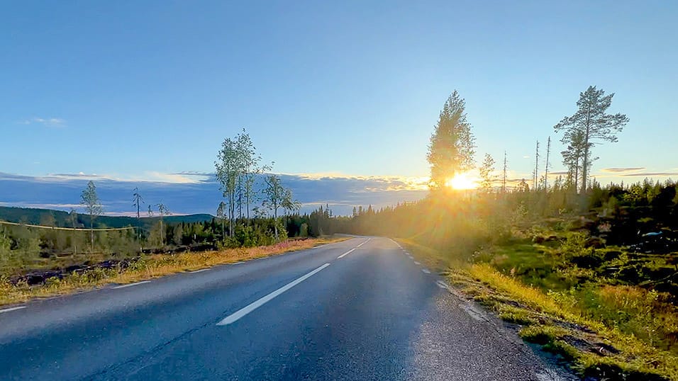 Sun glowing over a quiet forest road in northern Sweden during a bright evening