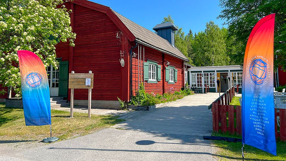 Red wooden building in Västerbotten Sweden with colourful Midnight Sun Randonnée flags at the entrance