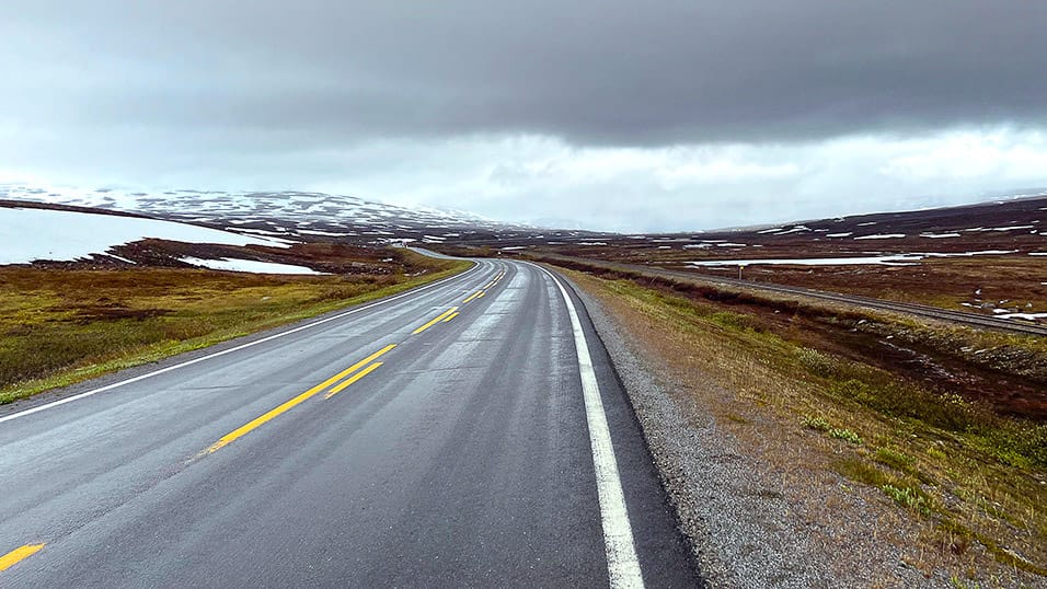 Wet plateau road with snow patches and wide open tundra in northern Sweden
