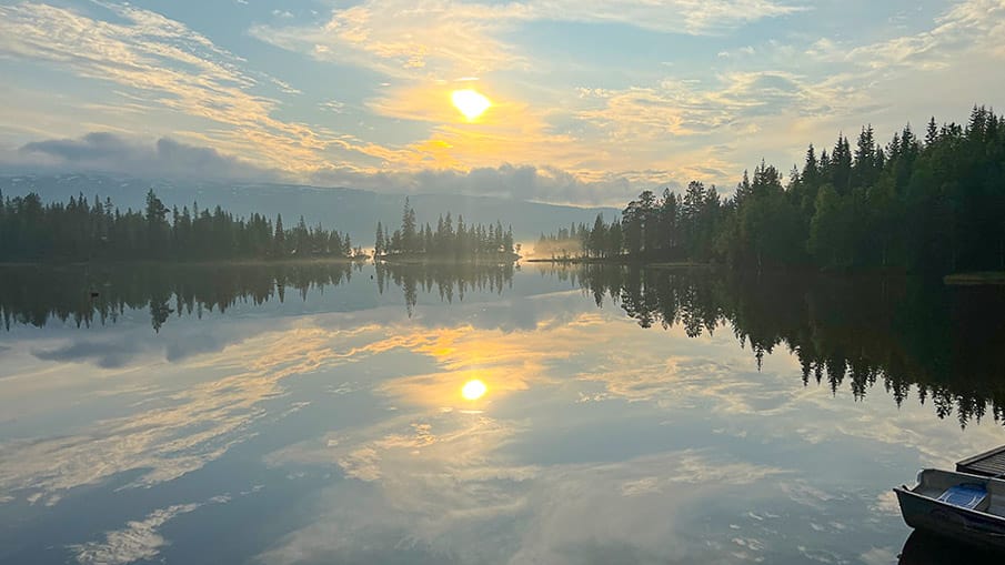 Sunset reflecting on the calm Vindel River in Västerbotten Sweden with forested banks and soft clouds