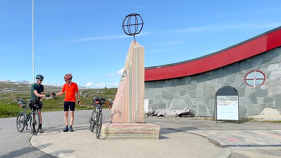 Cyclists standing with bikes beside the Arctic Circle monument in northern Sweden