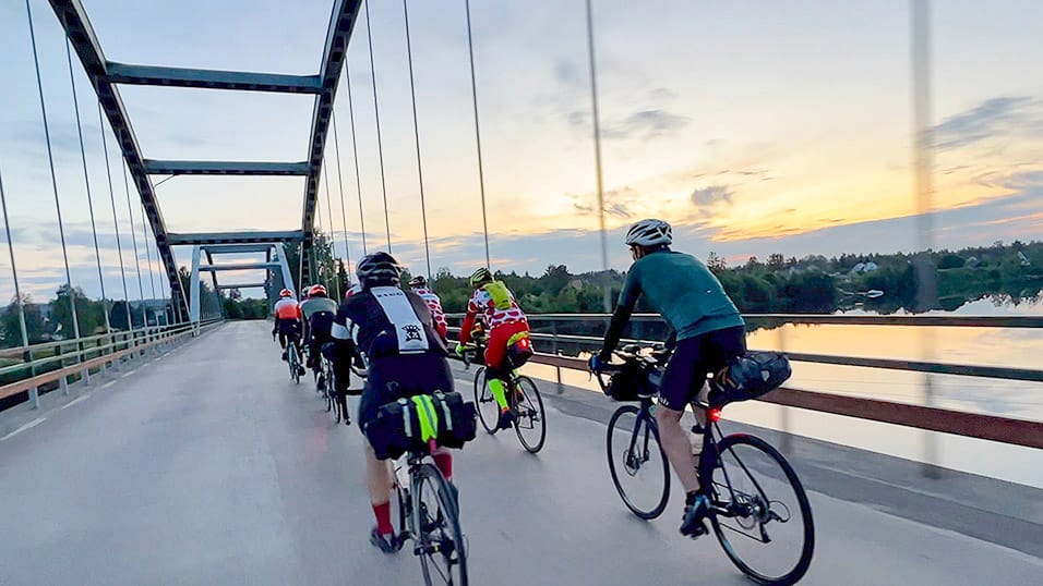 Cyclists crossing a bridge at sunrise during the Midnight Sun Randonnée in Västerbotten Sweden
