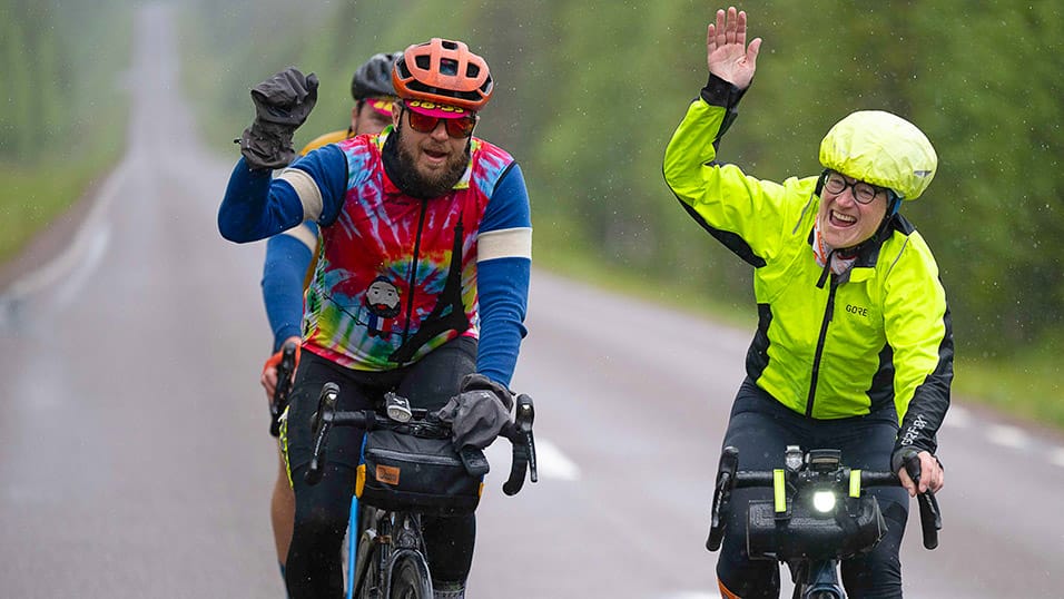 Cyclists riding in the rain and waving during the Midnight Sun Randonnée in Västerbotten Sweden