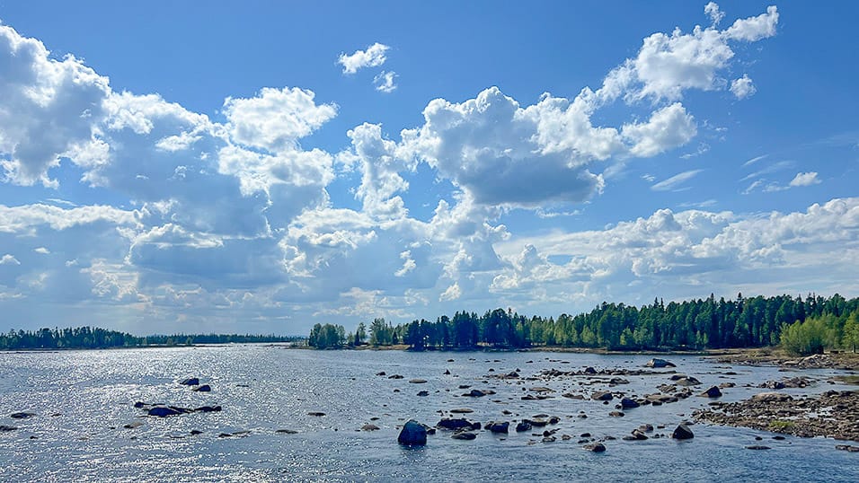 Rocky shoreline and forest beside wide lake in Västerbotten Sweden under bright clouds
