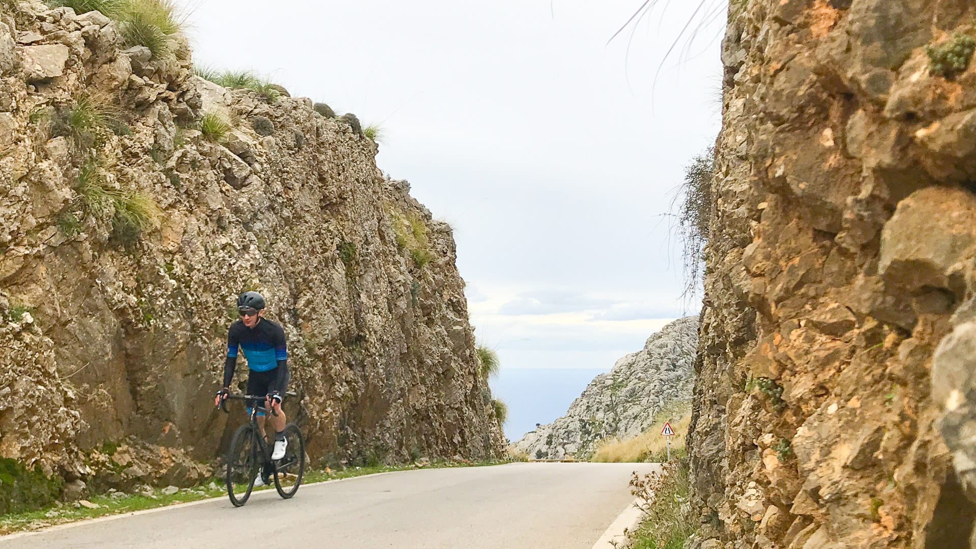 Cyclist climbing between rocky cliffs on the Sa Calobra road with sea views in Mallorca