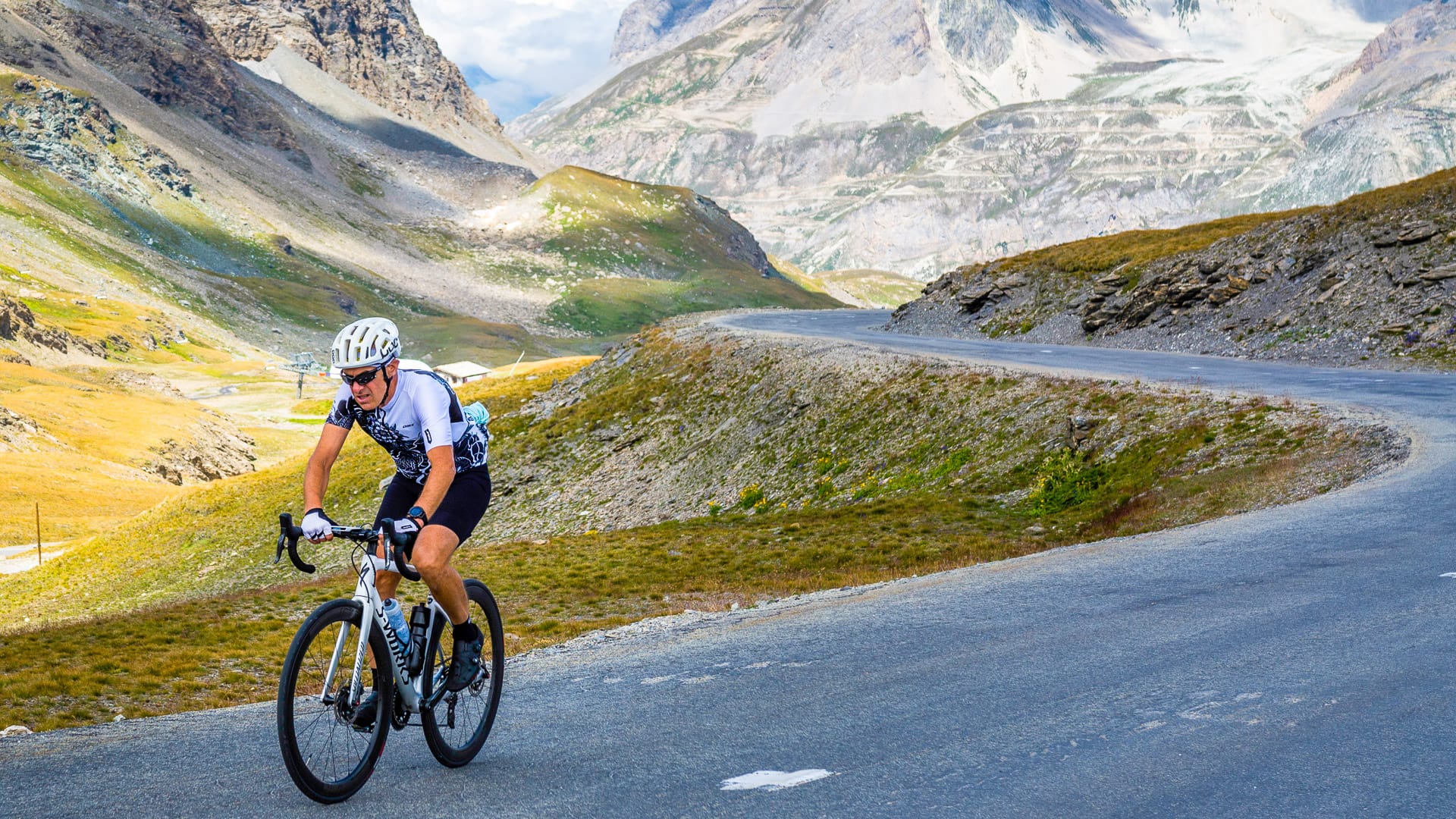 Cyclist climbing open alpine road with rugged mountain backdrop on the Route des Grandes Alpes
