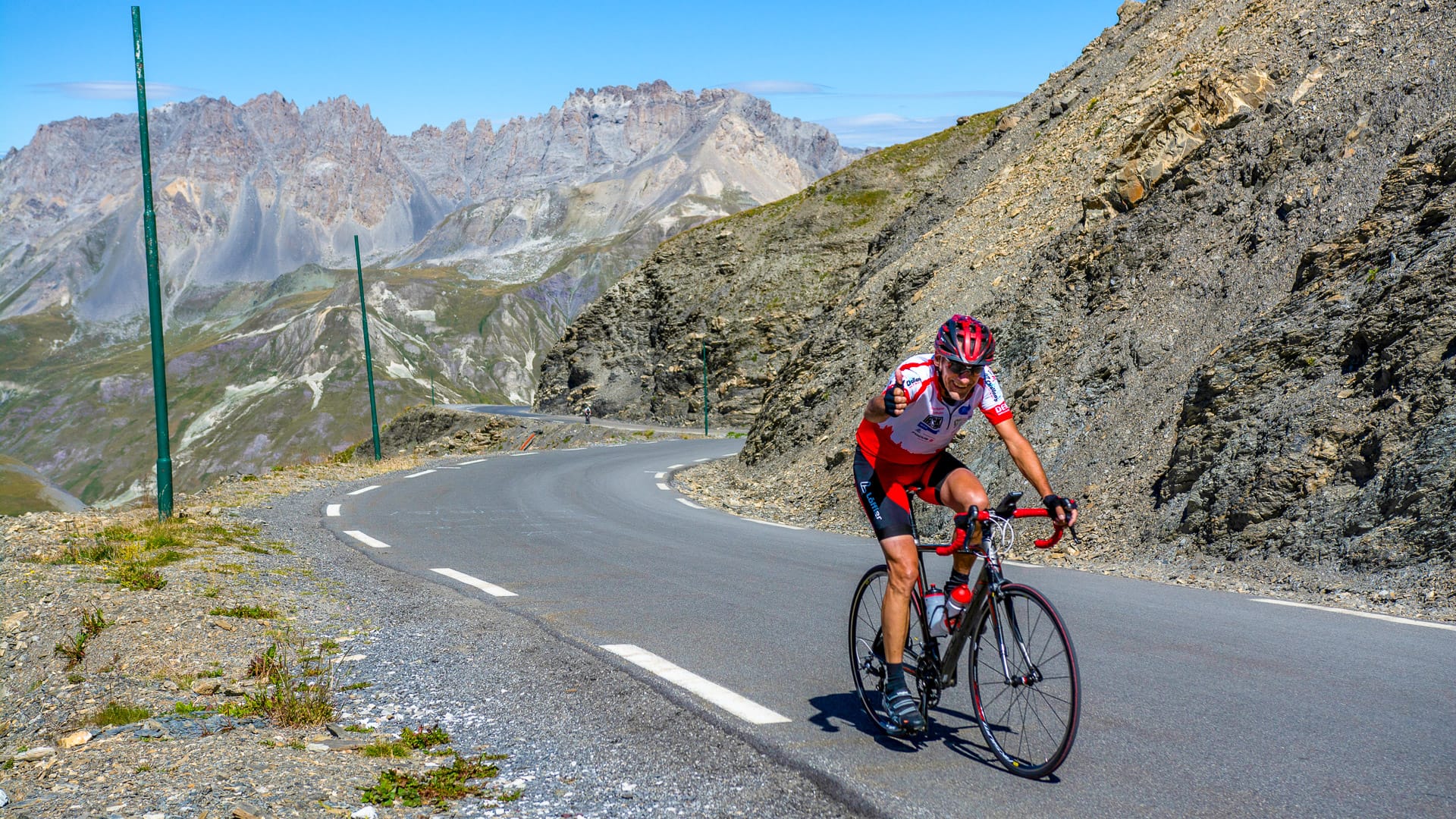 Solo cyclist ascending high alpine road on Route des Grandes Alpes with rugged mountain backdrop