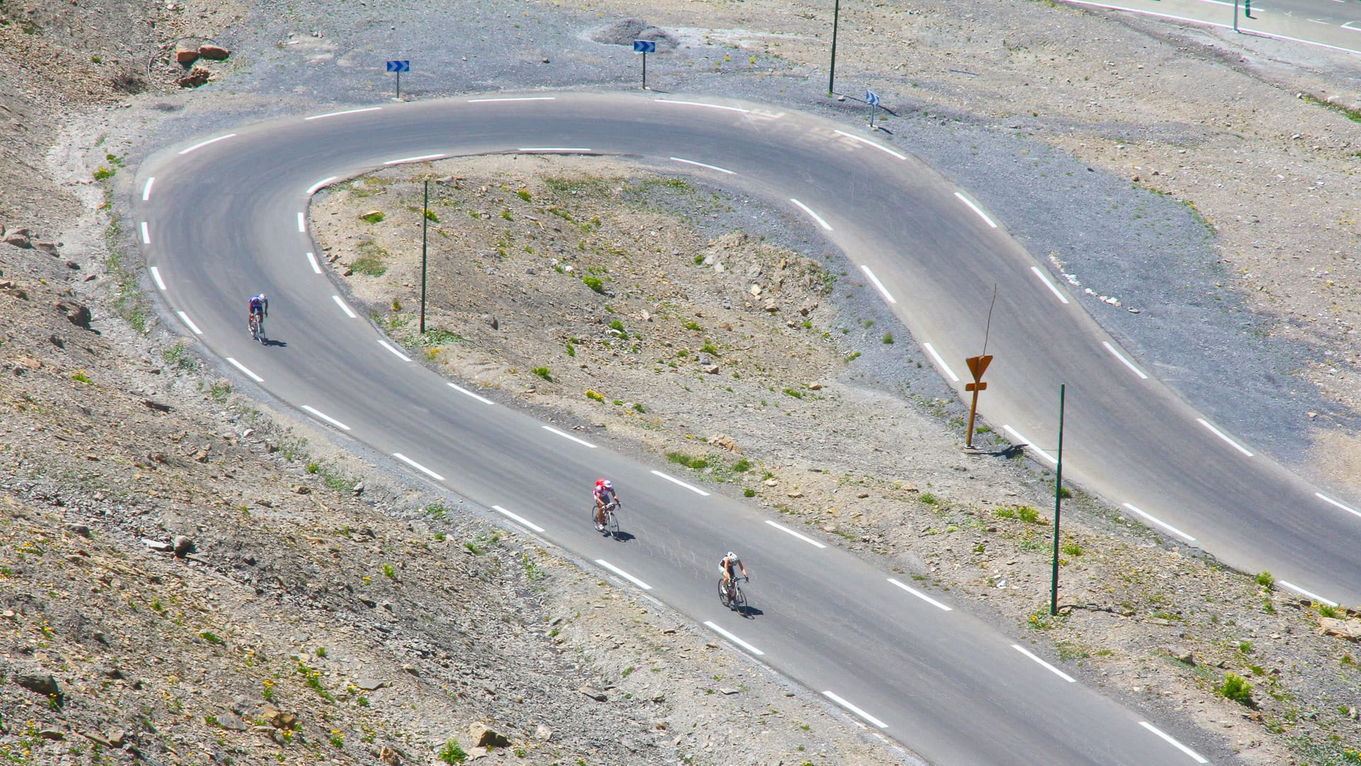 Cyclists rounding wide hairpin bend on barren alpine road along the Route des Grandes Alpes, France