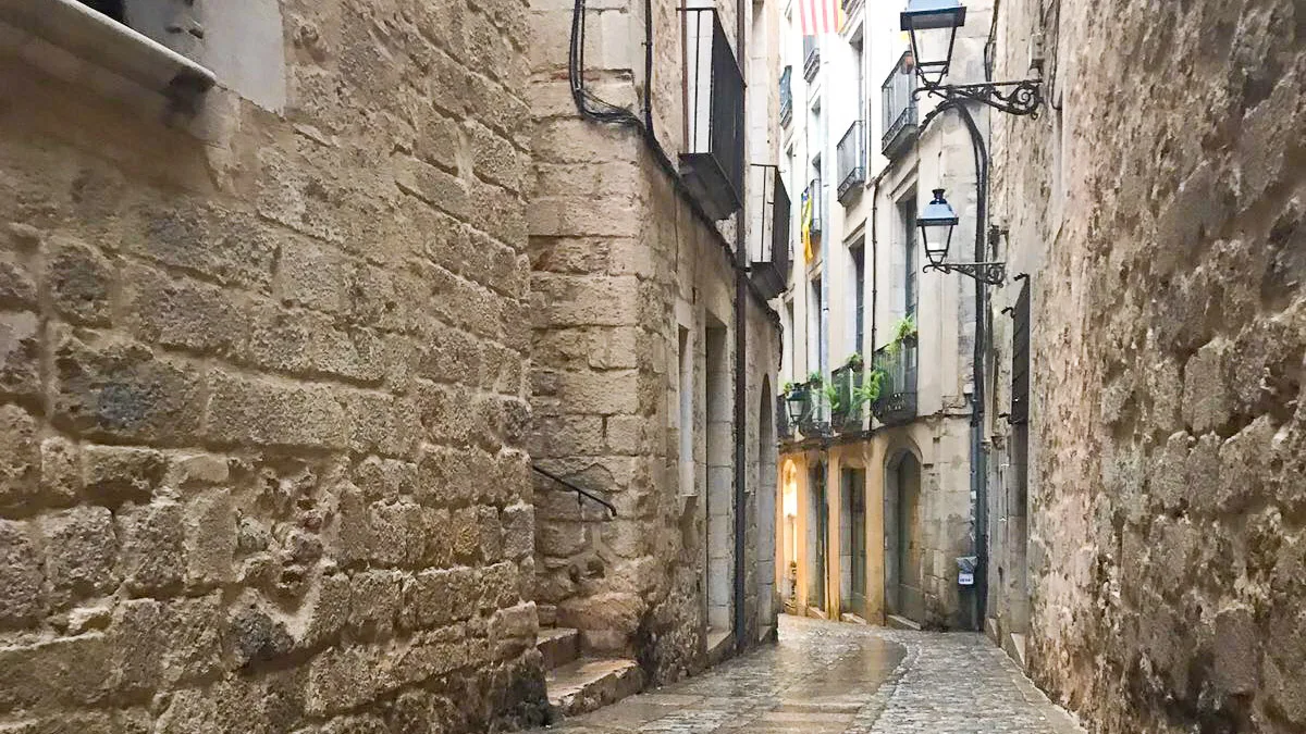 Narrow cobbled alleyway in Girona’s old town with historic stone buildings and wrought iron balconies