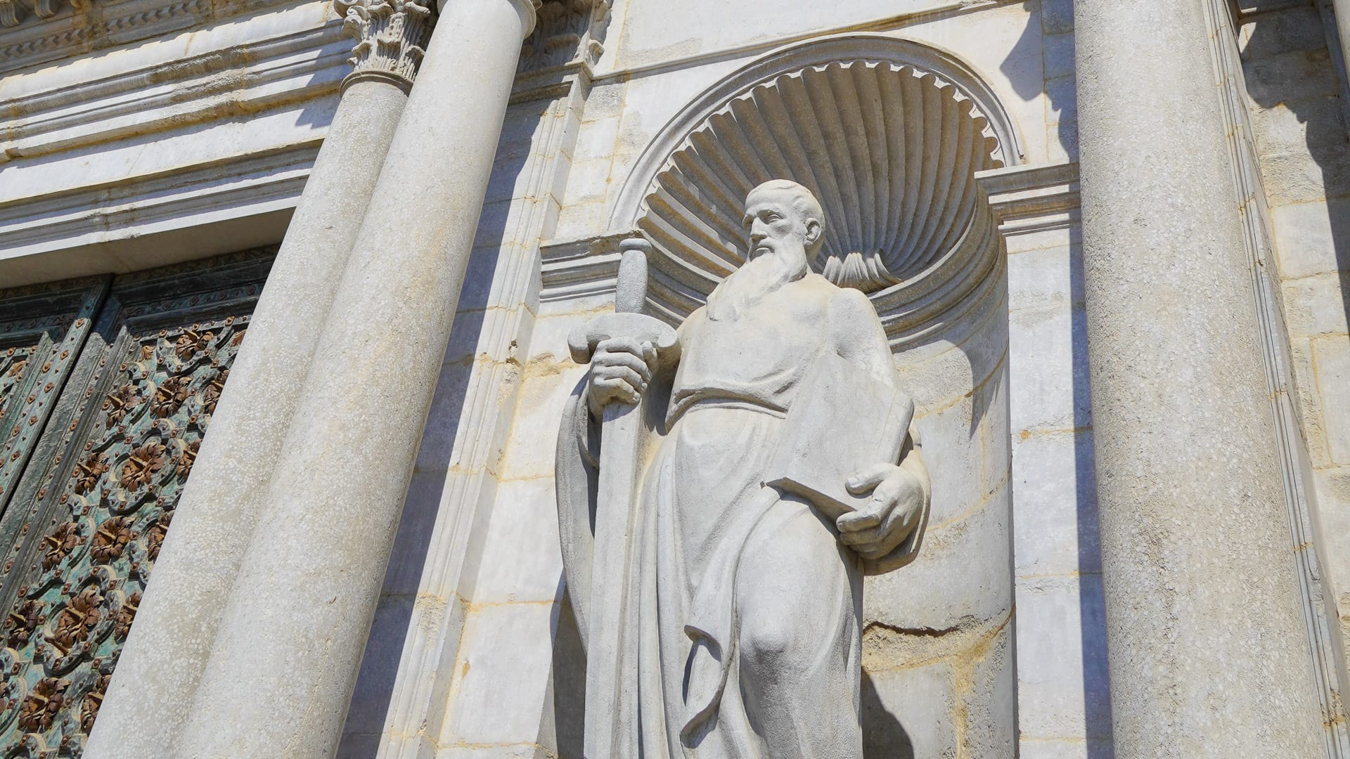 Close-up of stone statue in niche on Girona Cathedral façade holding scroll and book