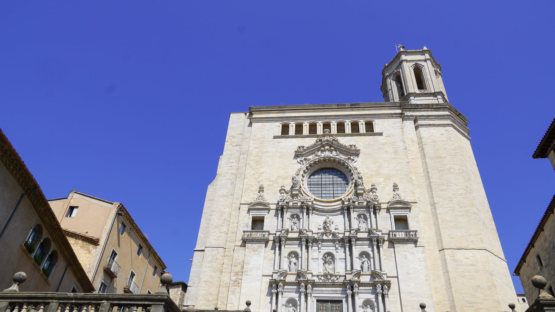 Baroque façade of Girona Cathedral with large central rose window and bell tower under clear blue sky