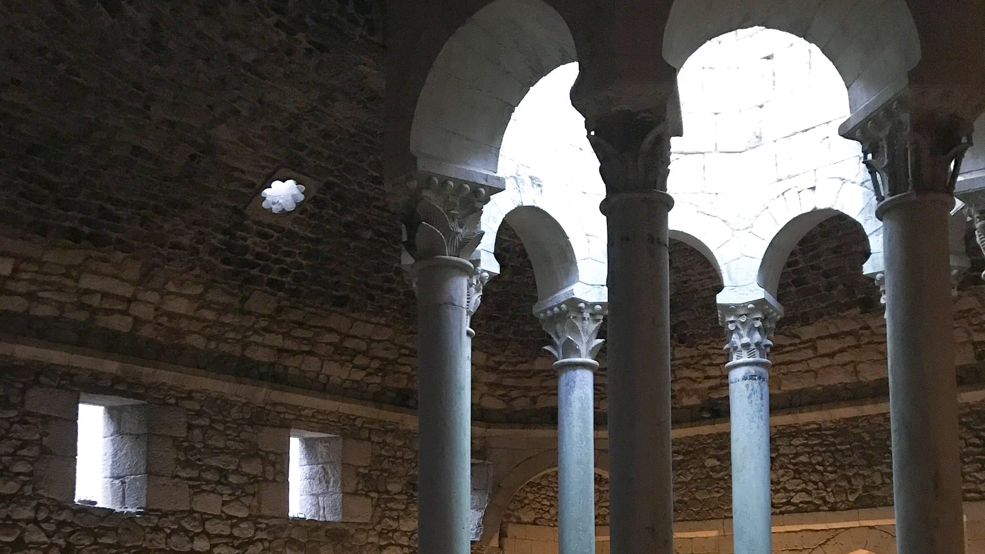 Interior of Arab Baths in Girona featuring Romanesque columns and dome with light filtering through openings