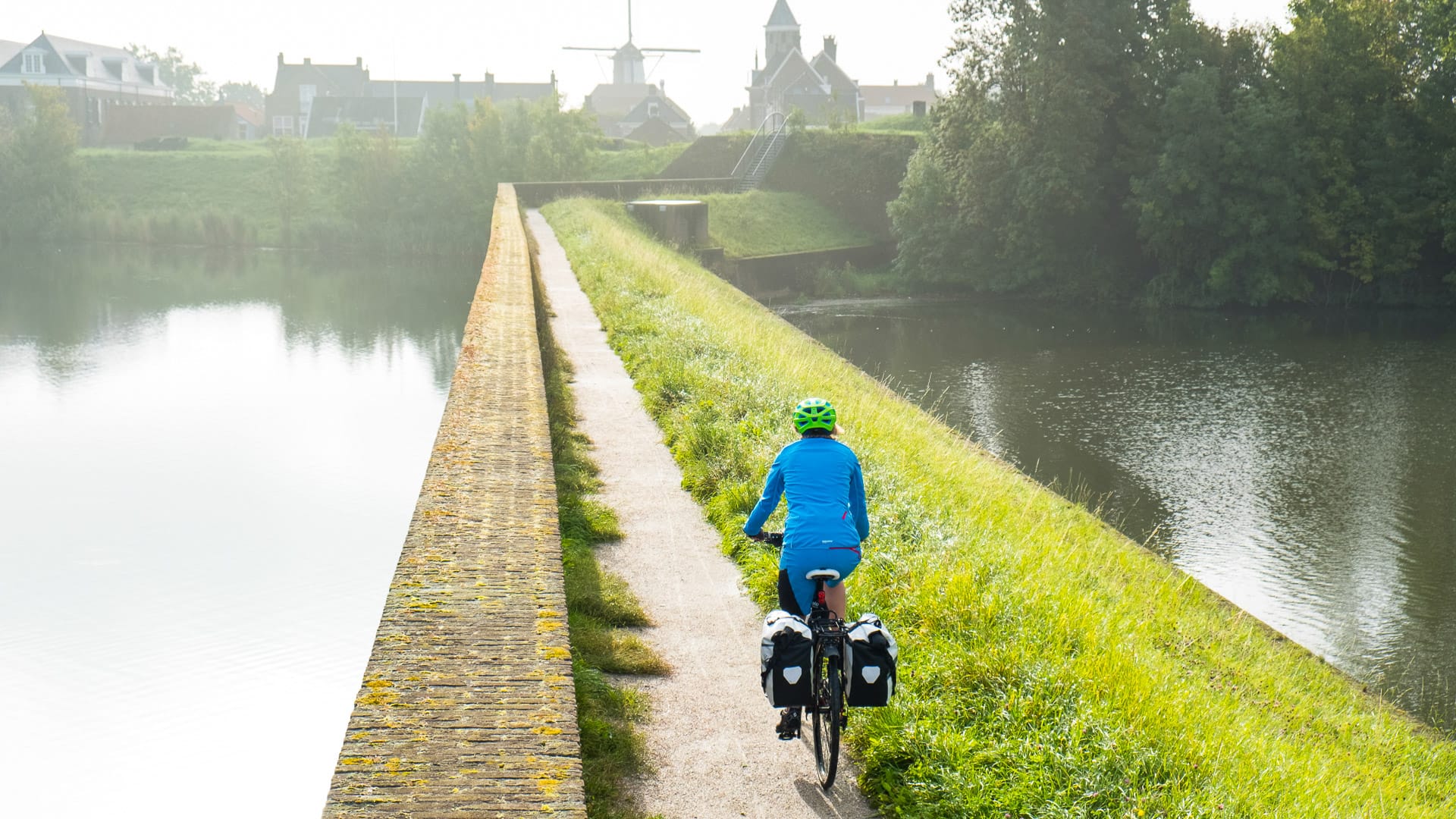 Touring cyclist on a dyke path near a fortified town on the Amsterdam to Bruges cycling route