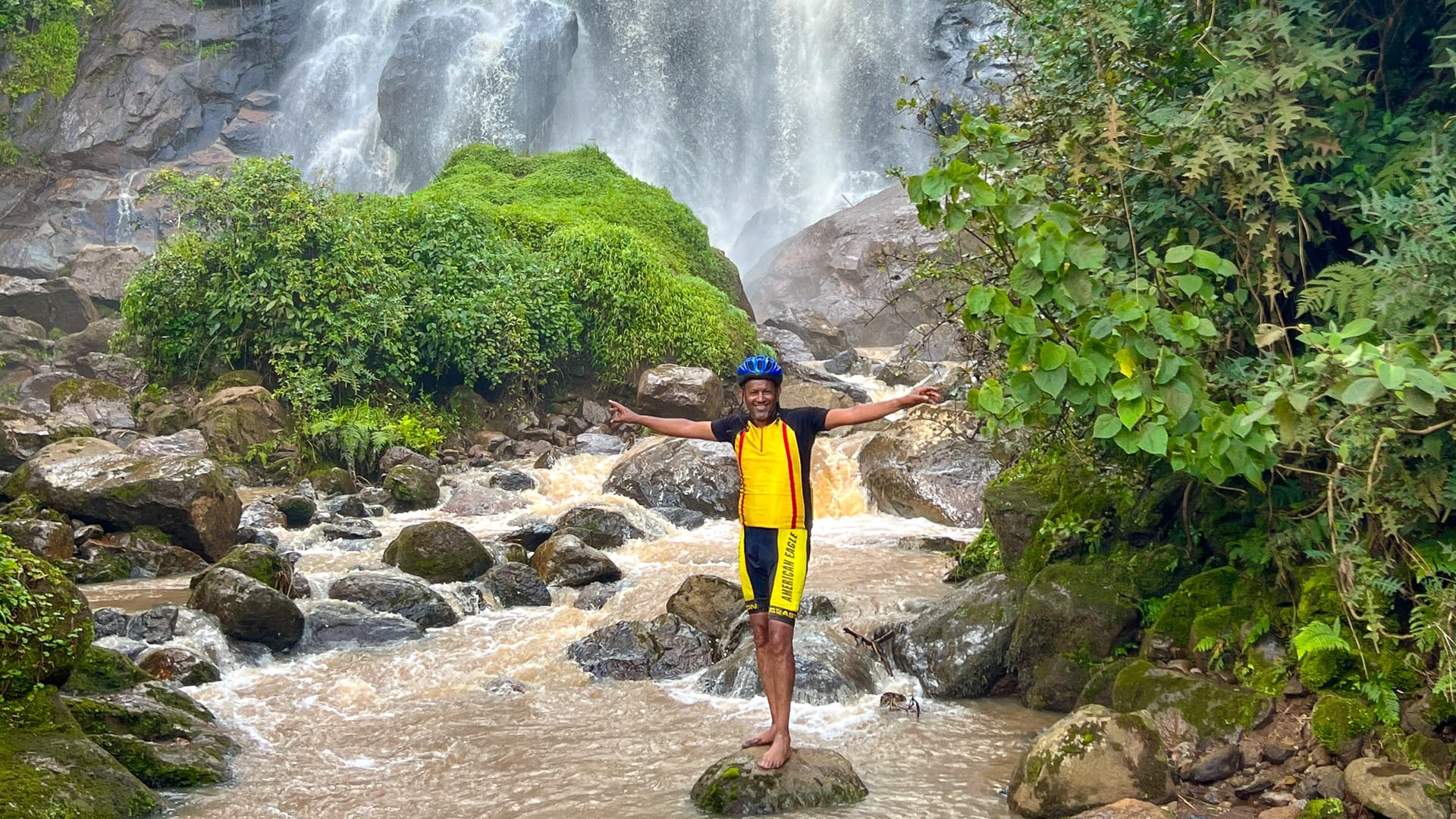 Cyclist standing in a river below a waterfall during a cycling trip in Ethiopia