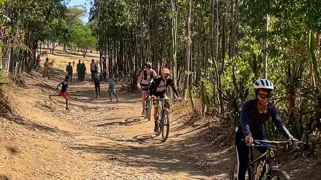 Cyclists riding along a shaded dirt track during a cycling trip in rural Ethiopia