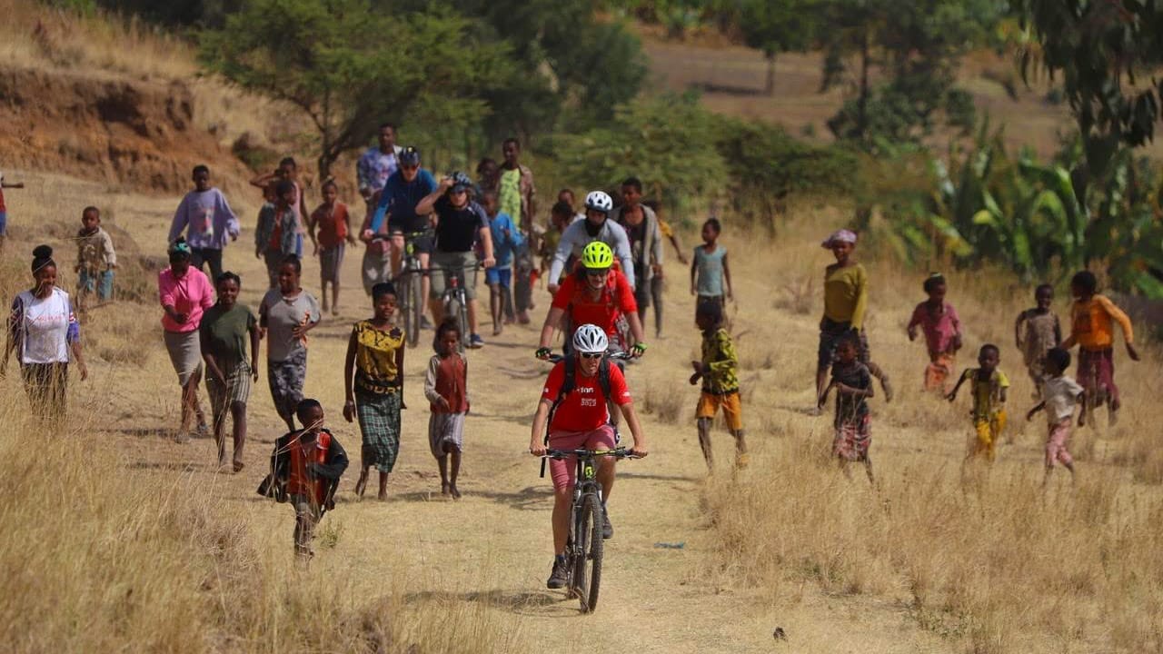 Cyclists riding through a rural village with local children during a cycling trip in Ethiopia