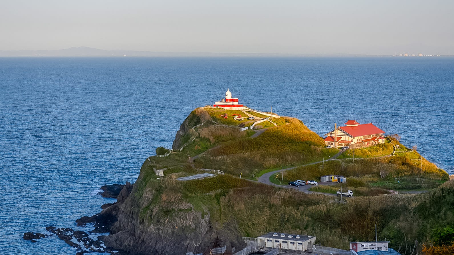 Red and white lighthouse on a green headland above the sea in Hokkaido Japan