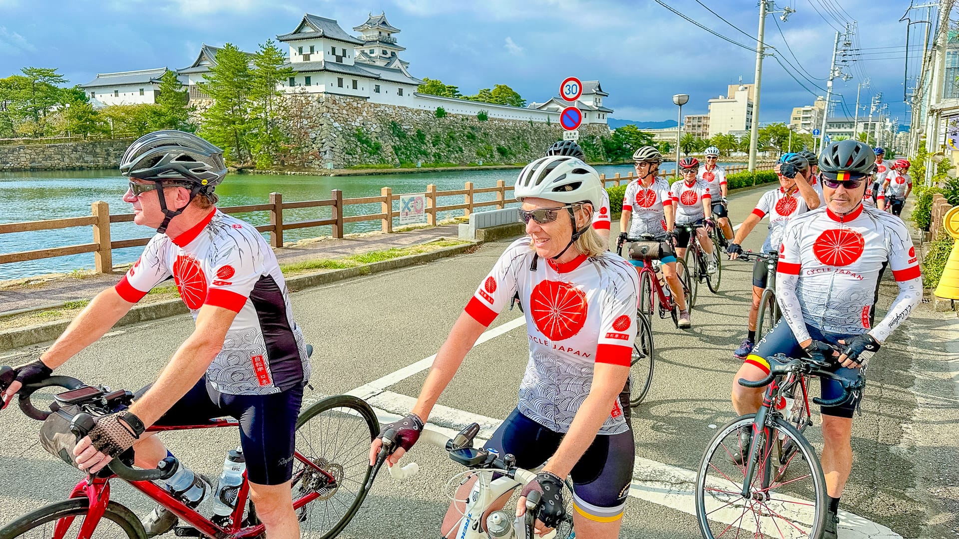 Group of cyclists in matching jerseys riding past Takaoka Castle in Kyushu Japan