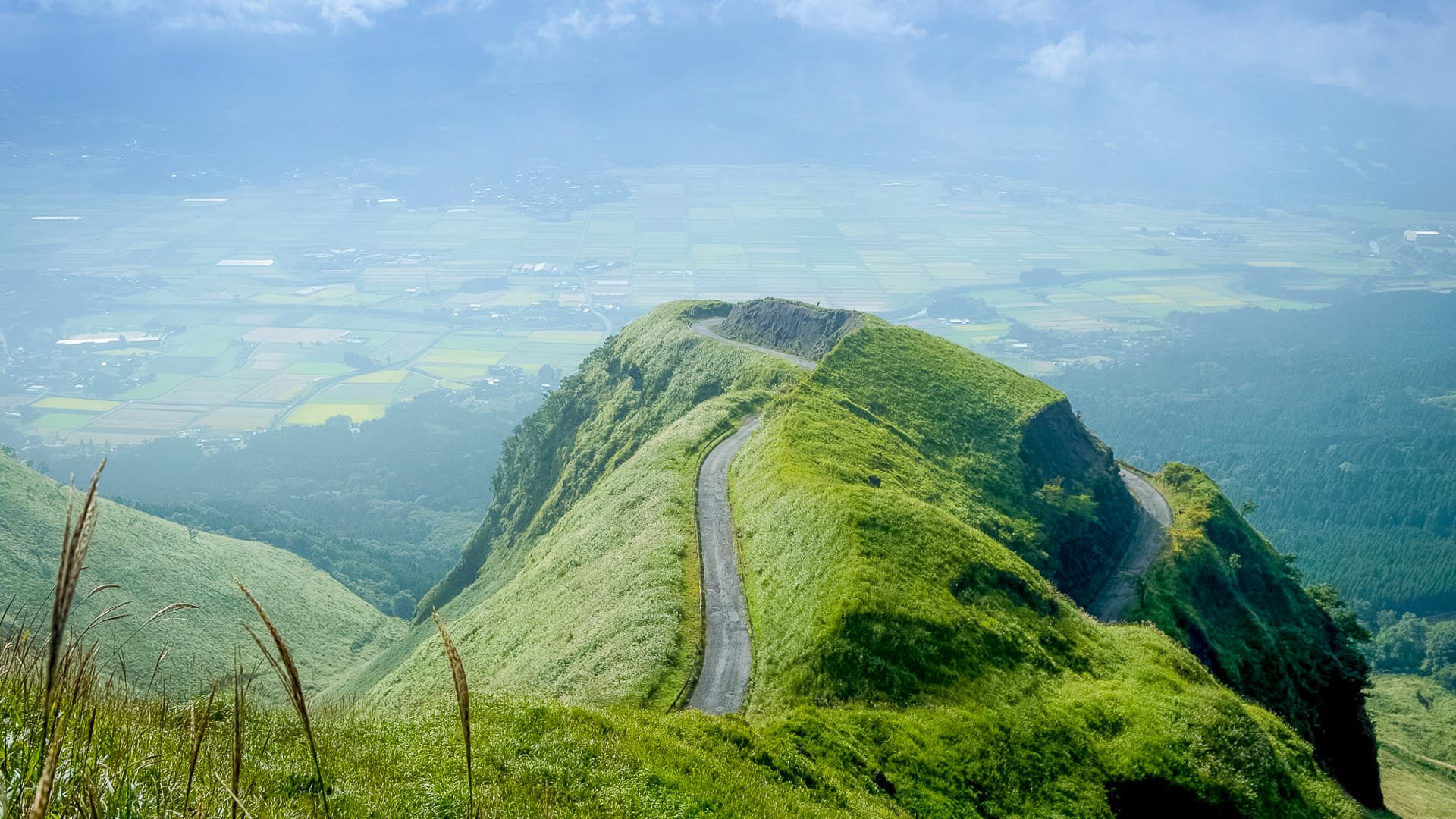 Winding road along lush green ridges of Mount Aso in Kyushu Japan with hazy valley views