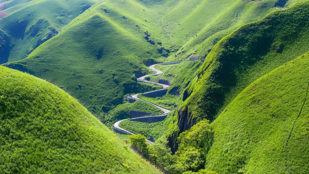 Serpentine road cutting through bright green hills of Mount Aso in Kyushu Japan