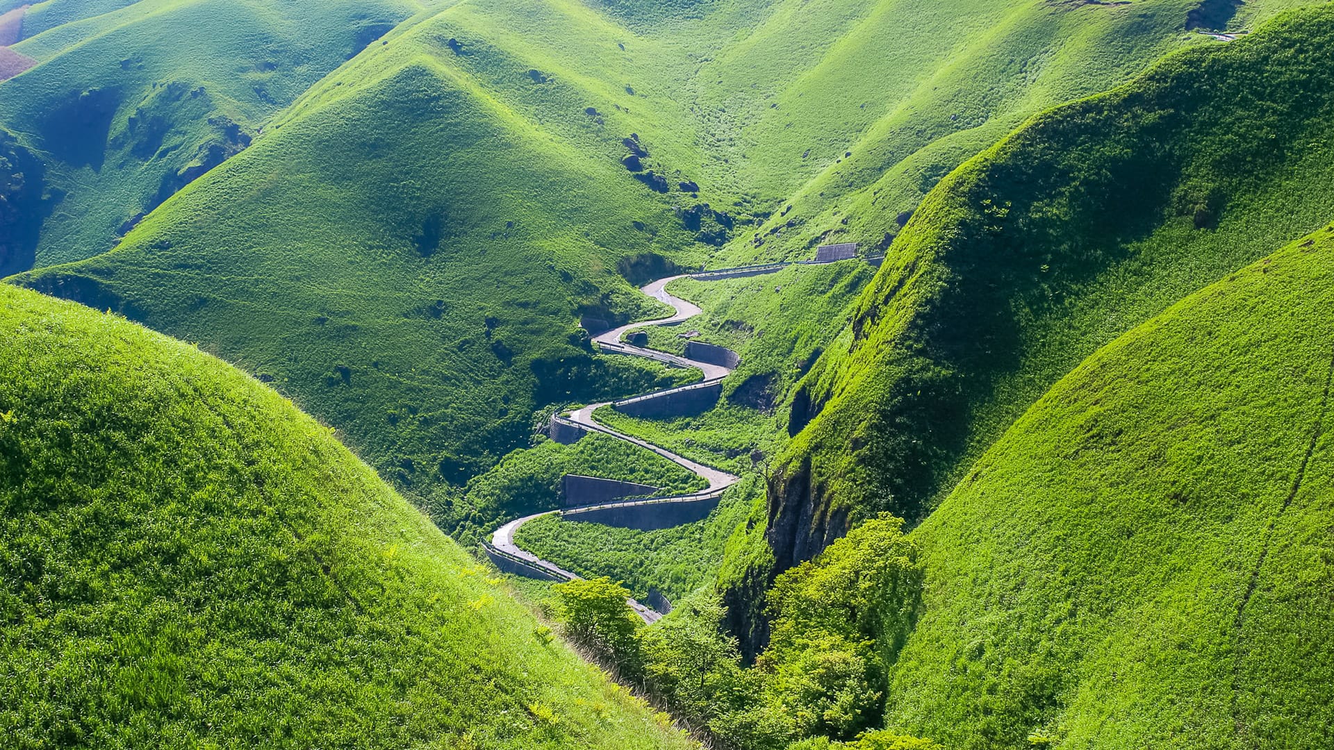 Serpentine road cutting through bright green hills of Mount Aso in Kyushu Japan