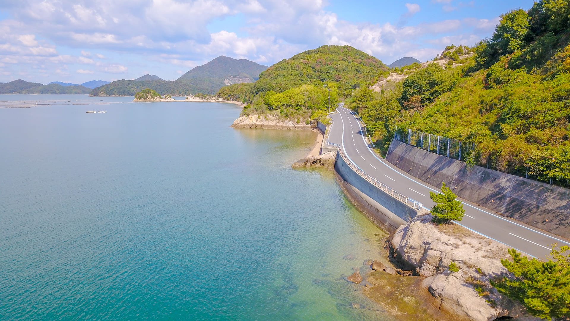 Coastal cycling road curving beside calm blue waters and green hills in Shimanami Kaido Japan