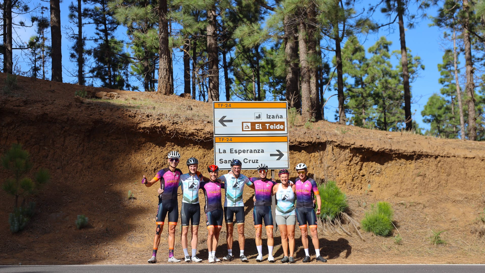 Group of cyclists posing by a road sign in a pine forest area of Tenerife