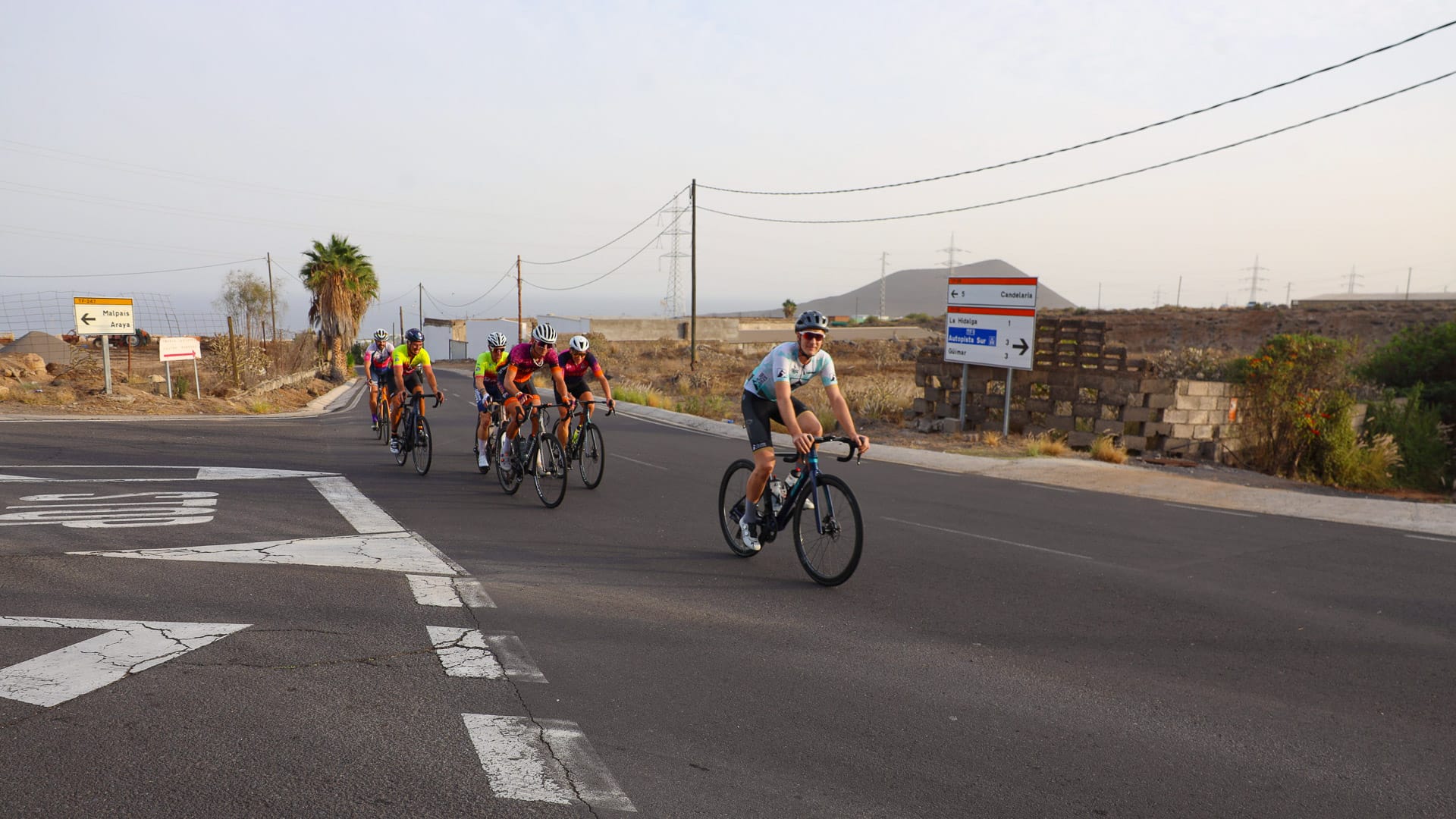 Group of cyclists riding through a road junction in southern Tenerife with dry volcanic scenery