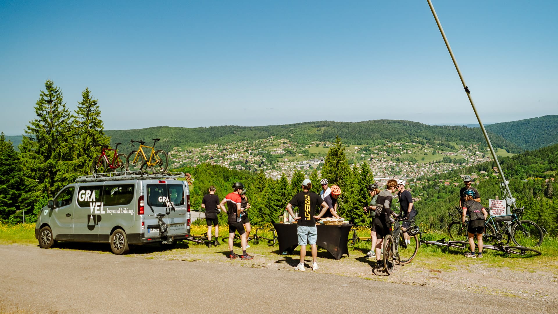 Cyclists taking a break by the support van with food table overlooking villages below in France
