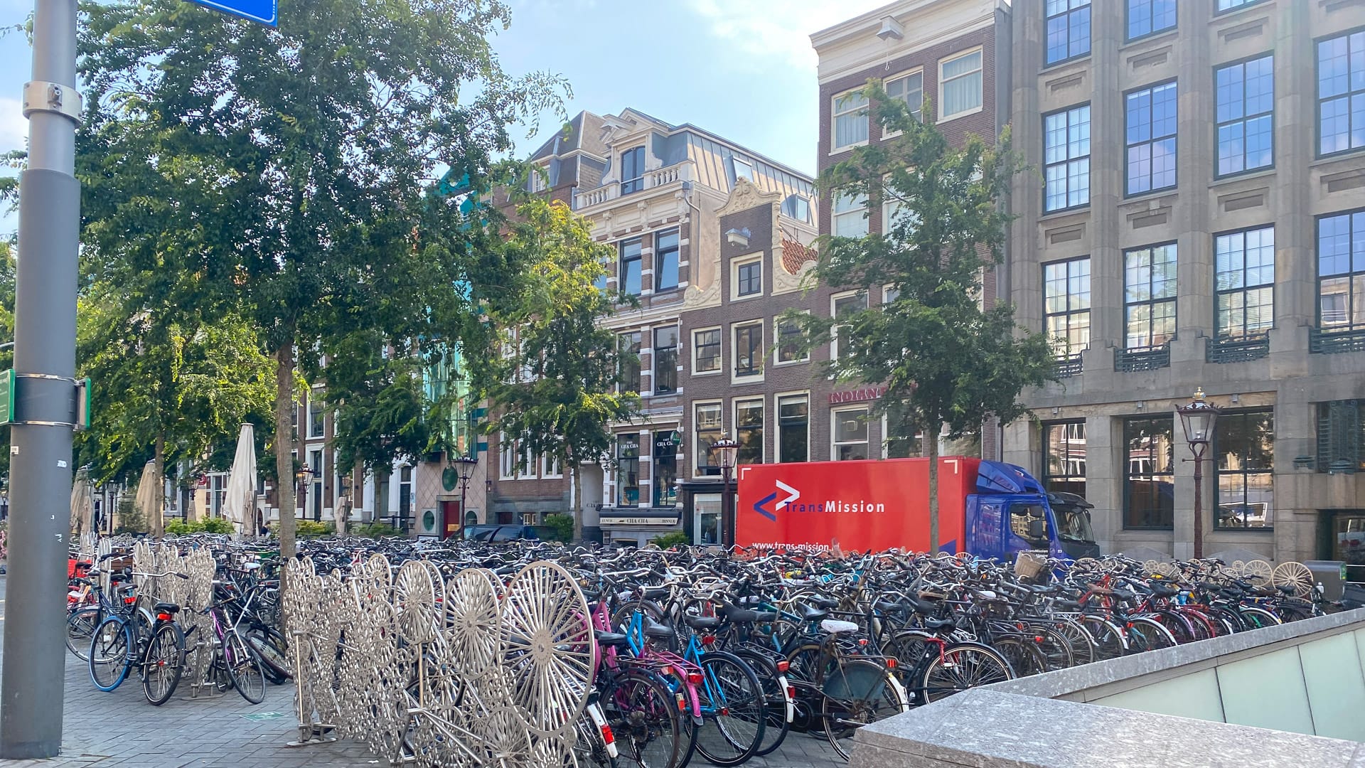 Rows of parked bicycles beside a canal in Amsterdam, with historic buildings and trees lining the street