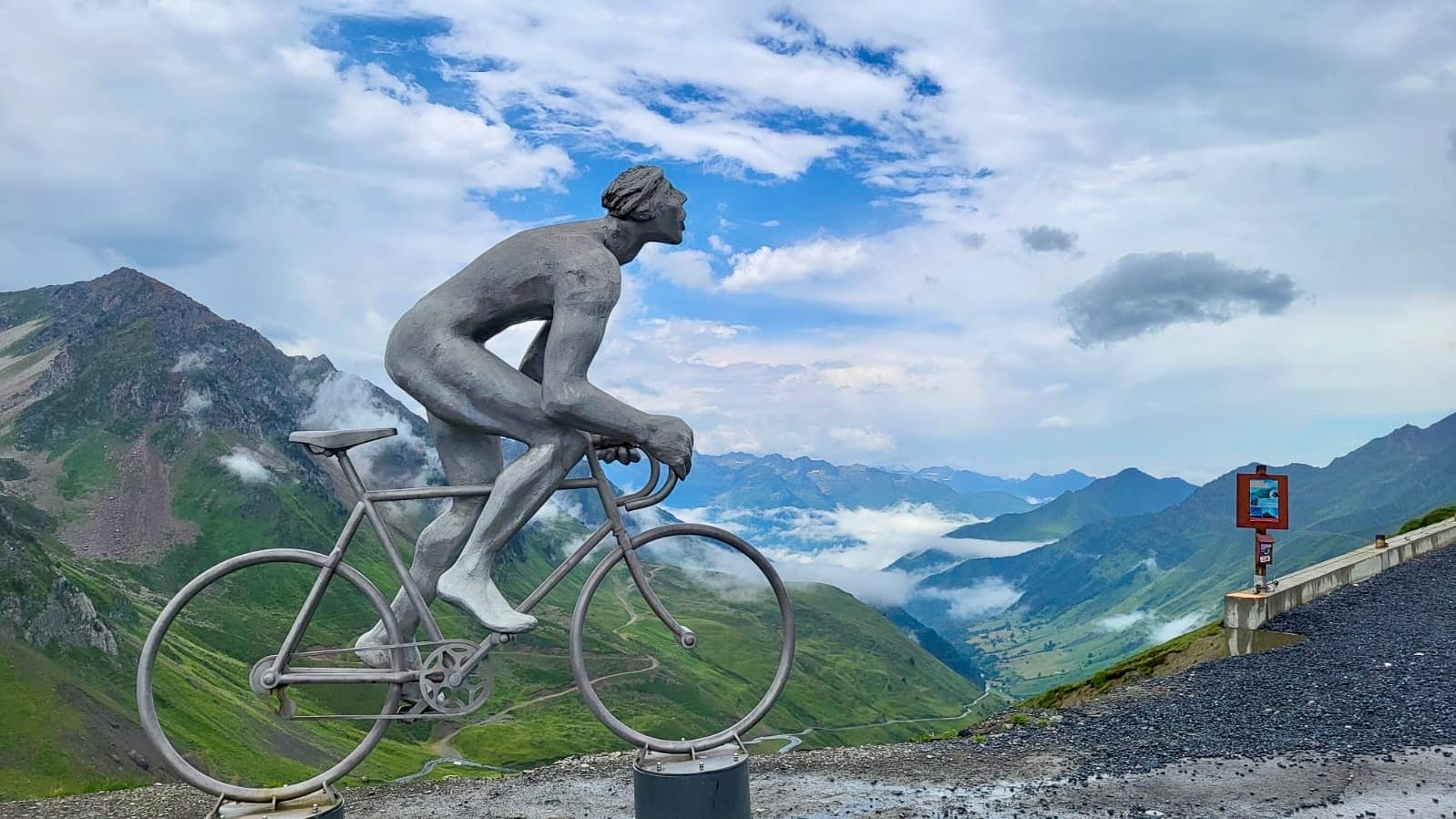 Giant cyclist monument on mountain summit along Tour de France route, misty peaks and valleys in French Pyrenees