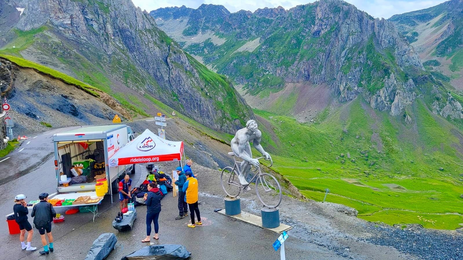 Cyclists and spectators around summit snack bar and giant cyclist statue on Tour de France route in the French Pyrenees