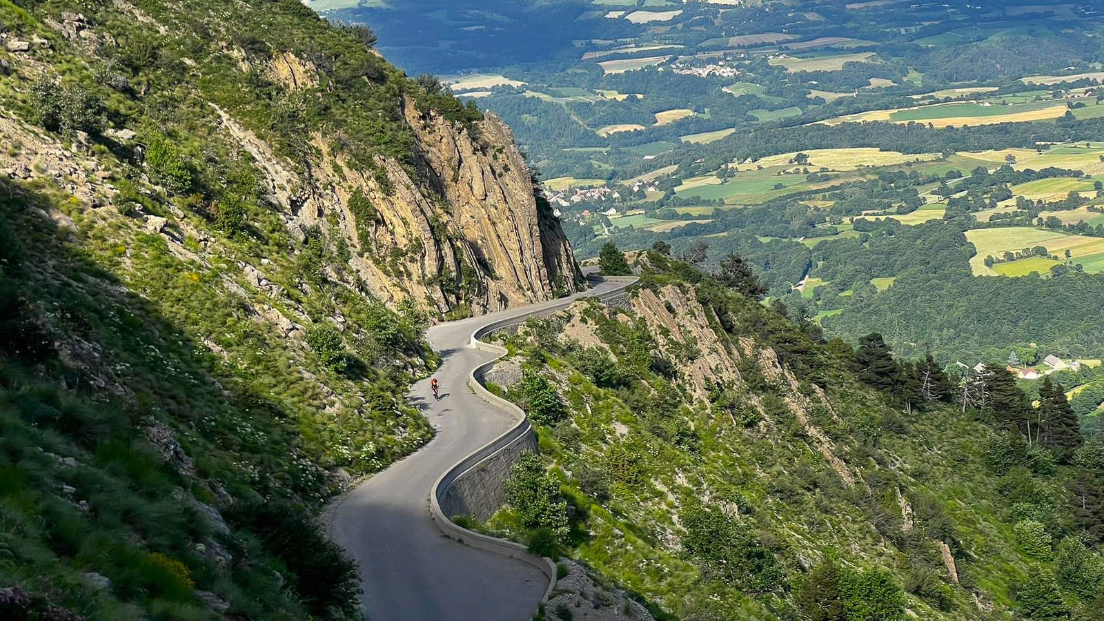 Dramatic balcony road on steep mountainside along Tour de France route, sweeping views over green French valley