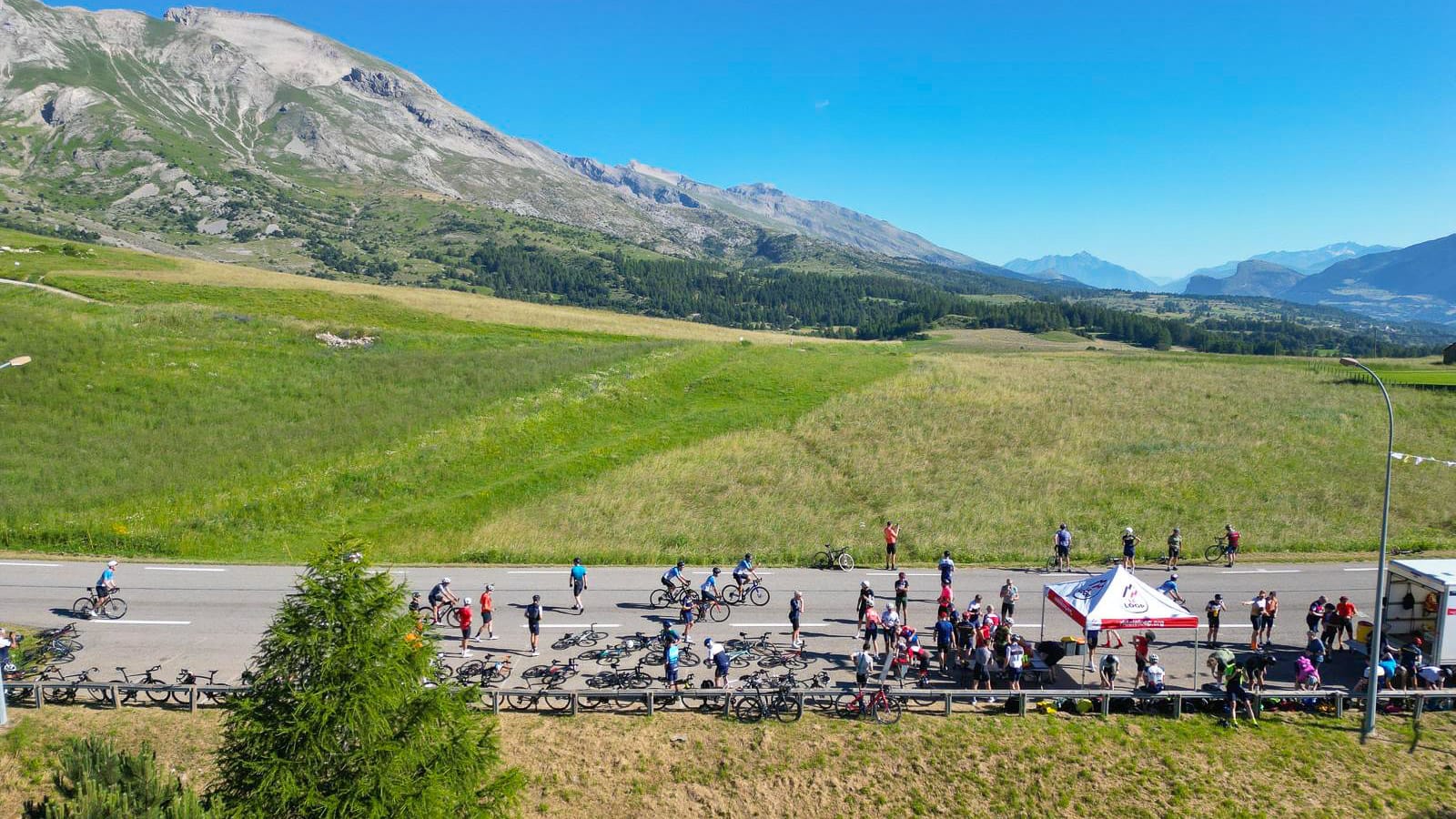 Cyclists climbing open mountain pass on Tour de France route, spectators lining roadside in the French Alps