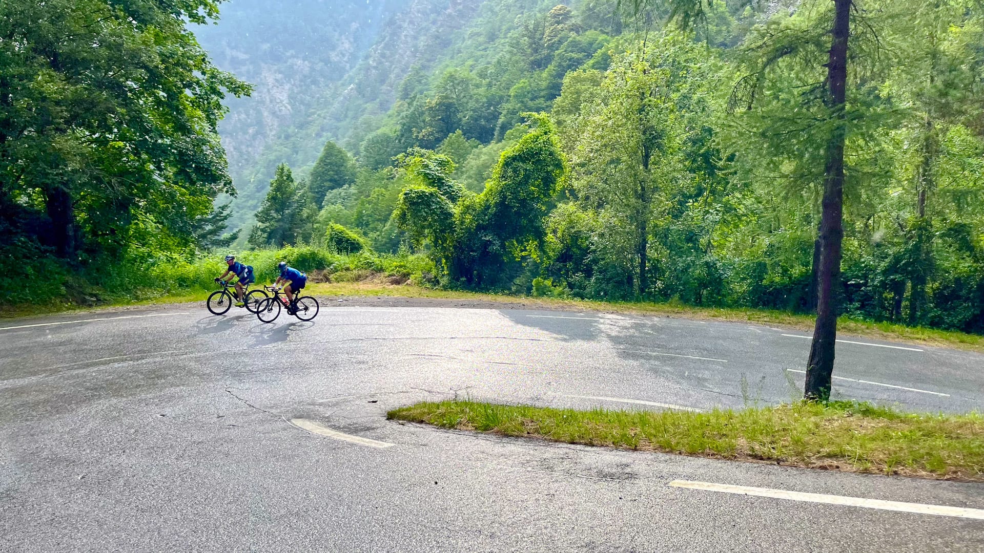 Two cyclists tackling wet forested hairpin bend on Tour de France route in the French mountains