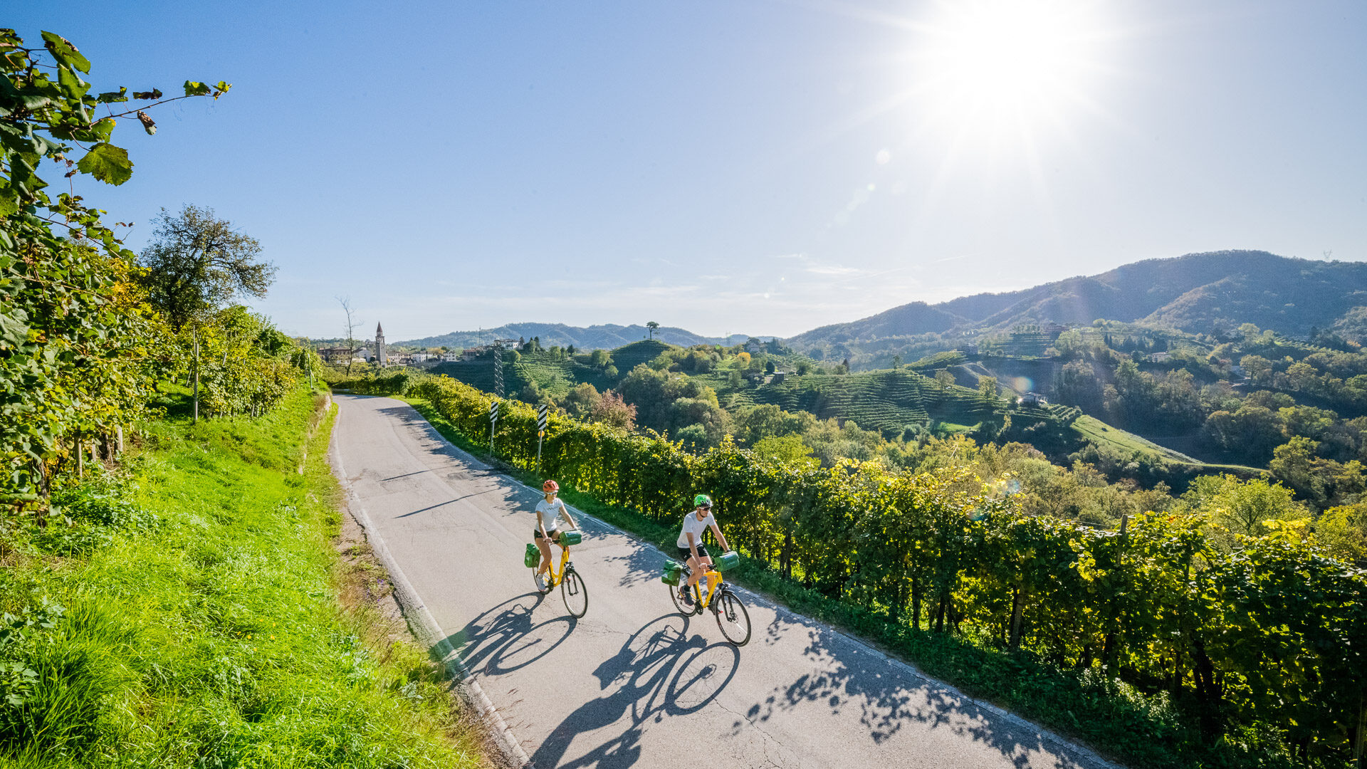 Two cyclsits on a quiet road in the Prosecco Hills, surrounded by vineyards
