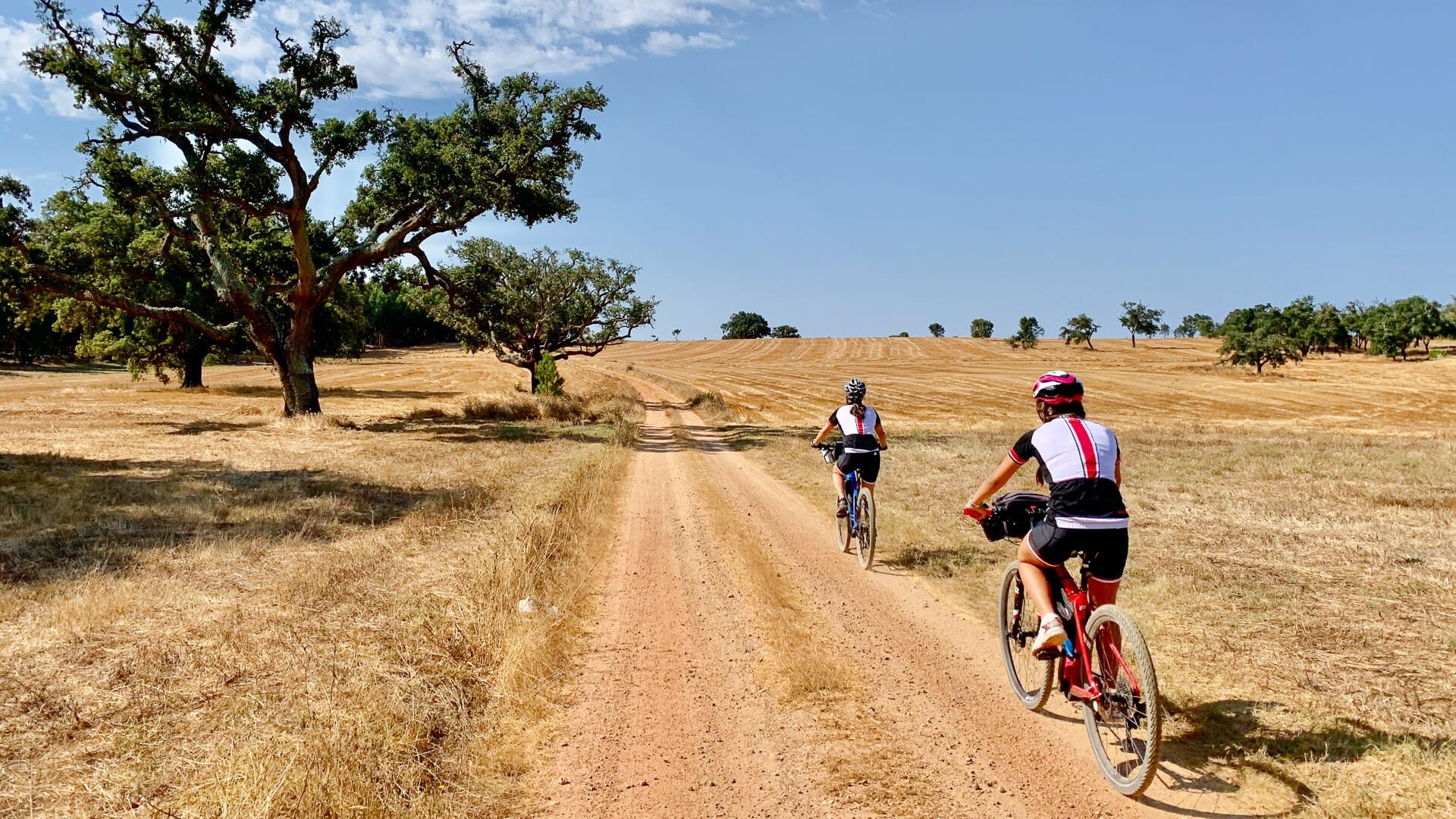 Cyclists riding under the sun on a red dirt section of the route in Alentejo, Portugal