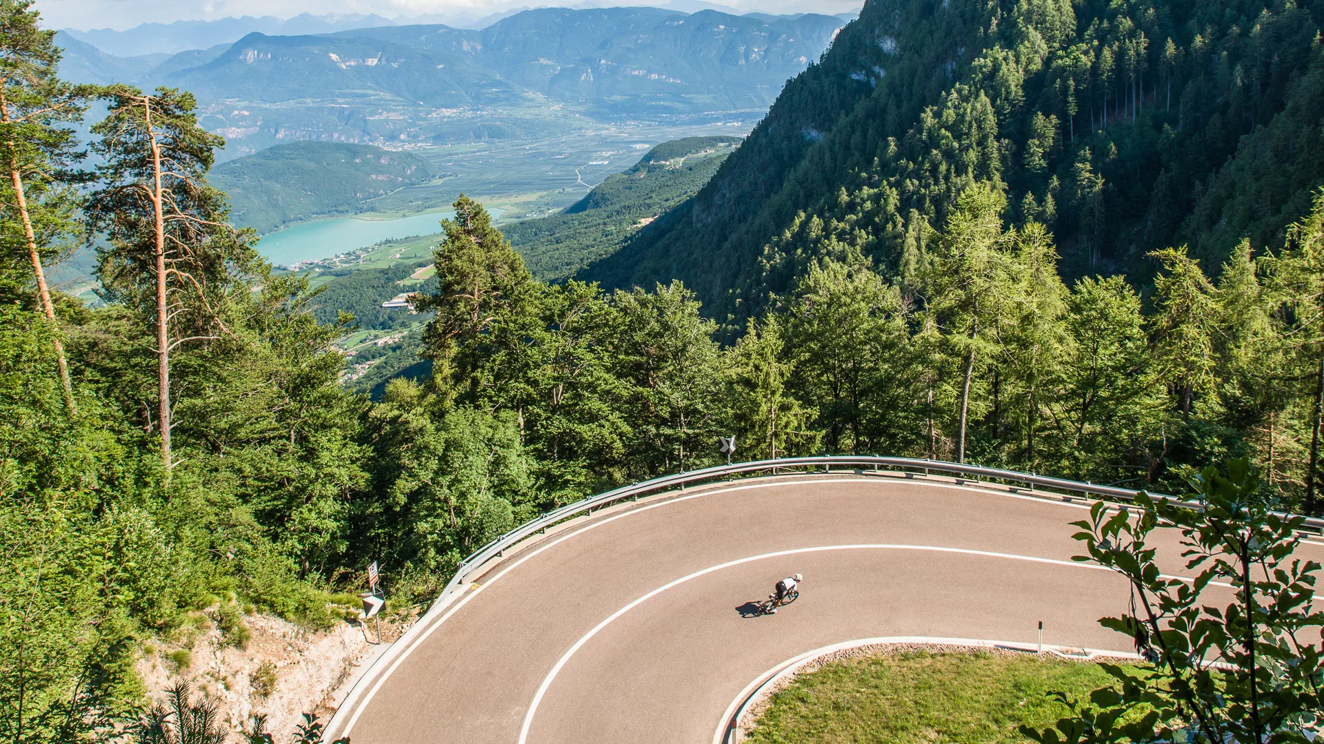 Cyclist taking a bend on a mountain road during the Giants of the Giro tour with lake and mountains in Italy