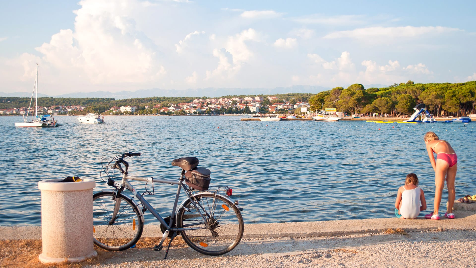 Two girls playing on a sea shore near a bicycle. View on a cozy little Croatian town Zadar covered in white fluffy clouds