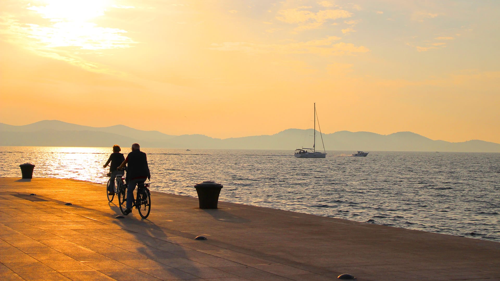 Silhouette Man and woman cycle along the waterfront in Zadar, Croatia with golden sunset, Europe