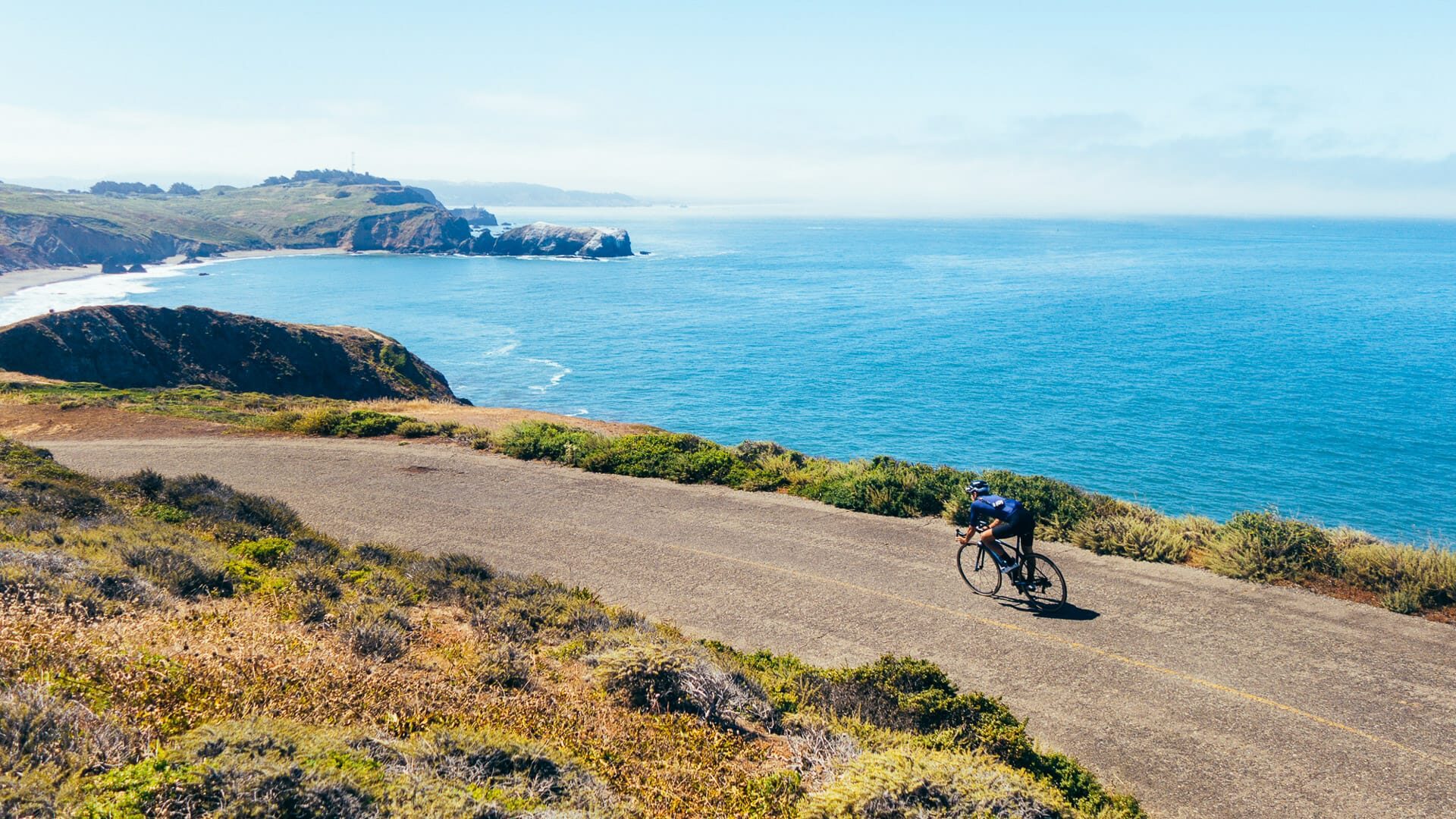 Slim fit strong male cyclist low aero riding fast on narrow road along the water toward beach