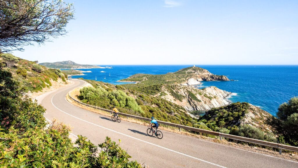 Two cyclists riding along a coastal road in Sardinia with sea views